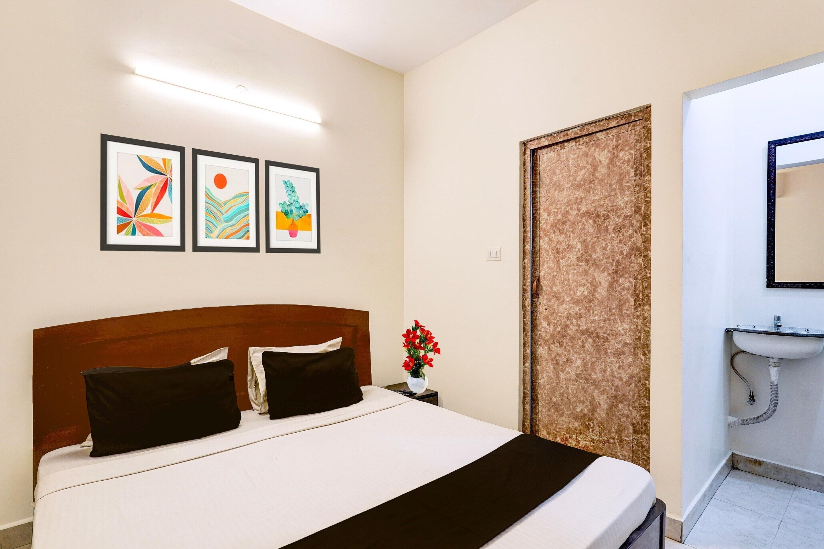 Una camera d'hotel con un letto, un comodino con un vaso di fiori e un bagno con lavandino e specchio.
