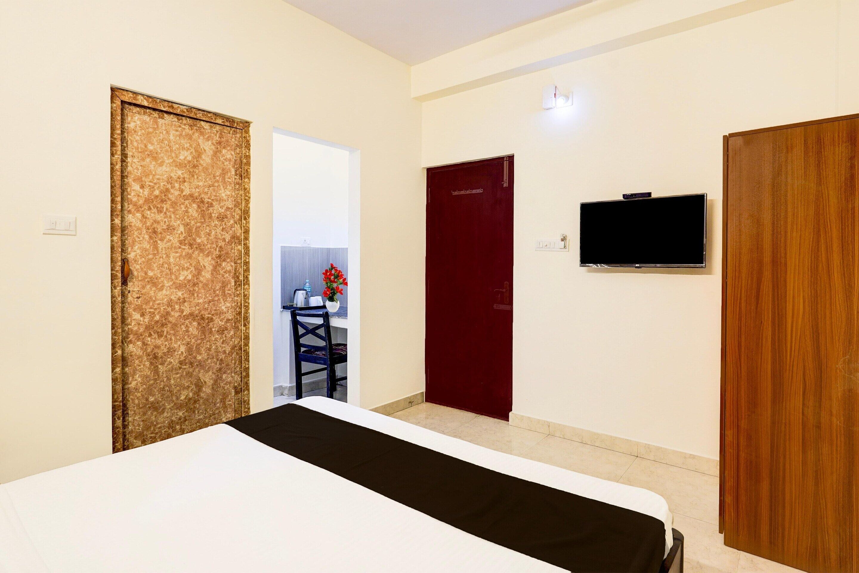 A hotel room with a bed, a TV, a red door, and a wooden door.