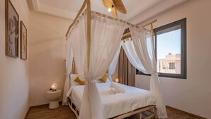 Ein Schlafzimmer mit Himmelbett, Nachttisch, Fenster und Blick auf Gebäude.
