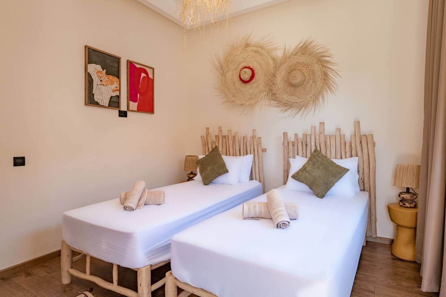 A hotel room with two single beds, wooden headboards, white bedding, a small table, and a wall-mounted artwork.