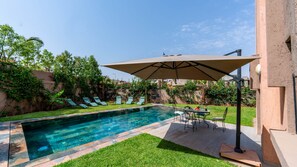 A swimming pool with lounge chairs and a table, surrounded by a well-maintained lawn and a stone wall. - Flextay - VILLA Lounge - 4Ch - Pool - Billiards (Marrakesh)