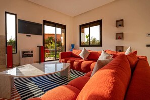 A modern living room with a large orange sofa, a glass coffee table, and a striped rug. - Flextay - VILLA Lounge - 4Ch - Pool - Billiards (Marrakesh)
