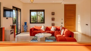 A modern living room with a red sofa, a coffee table, a large window, and a TV mounted on the wall. - Flextay - VILLA Lounge - 4Ch - Pool - Billiards (Marrakesh)