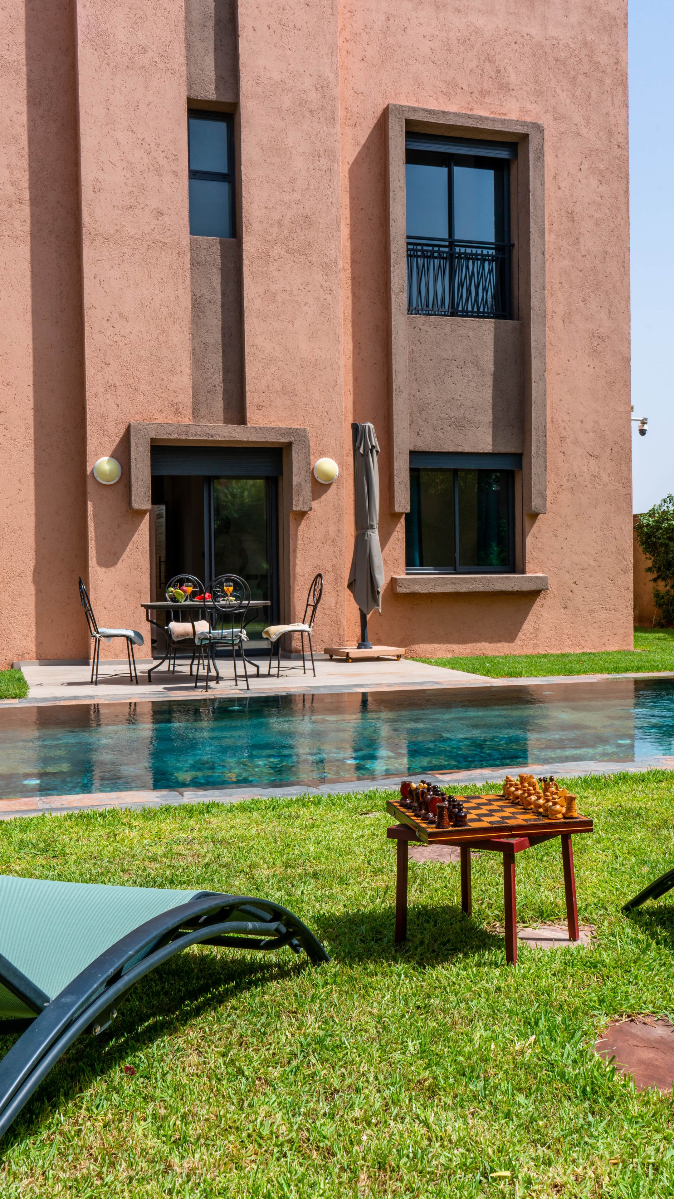 A modern building with a pool, outdoor seating, and a chess table.