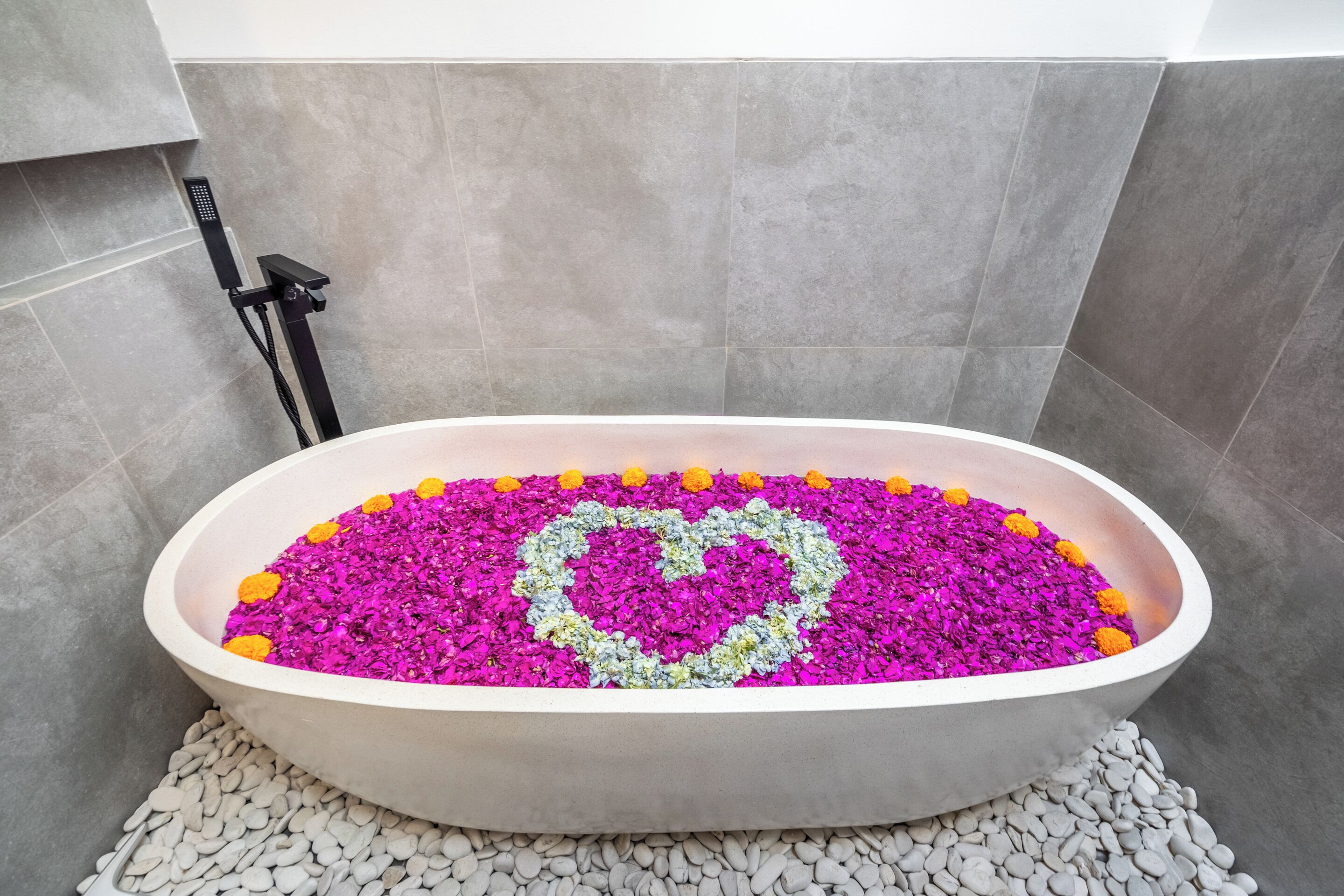 A bathtub filled with colorful flowers and a heart-shaped design, surrounded by gray tiles.