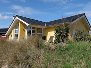 A yellow house with a sloped roof, large windows, and a chair outside. - 4 Star Holiday Home in Grossenbrode (Grossenbrode)