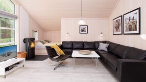 Uma sala de estar moderna com um sofá de couro preto, uma mesa de centro branca, uma cadeira preta, lareira e quadros nas paredes.