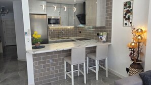 A modern kitchen with grey tiles, stainless steel appliances, and pendant lighting. - Sunny Poolside Modern Apartment in Tenerife South (CN)