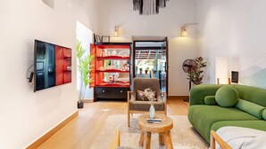 En moderne stue med et fladskærms-tv, en grøn sofa, et rødt reolsystem og loft i træ.