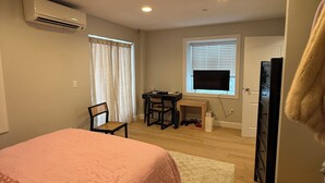 Un dormitorio con cama, escritorio, silla, aire acondicionado, televisor y puerta.