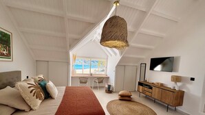 Una camera da letto con un letto, una scrivania, una TV e vista sulla spiaggia.