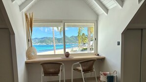 Una stanza con una scrivania, due sedie, vista su una spiaggia e un letto.