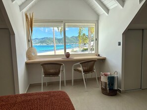 Ein Zimmer mit Schreibtisch, zwei Stühlen, Blick auf einen Strand und einem Bett.
