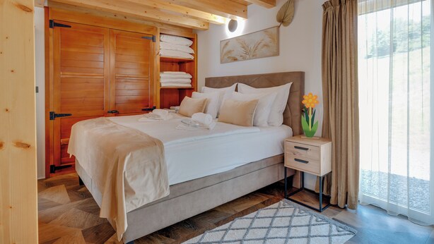A bedroom with a bed, wooden wardrobe, bedside table, and a window with curtains. - Plitvice Nature Resort (Plitvička Jezera)