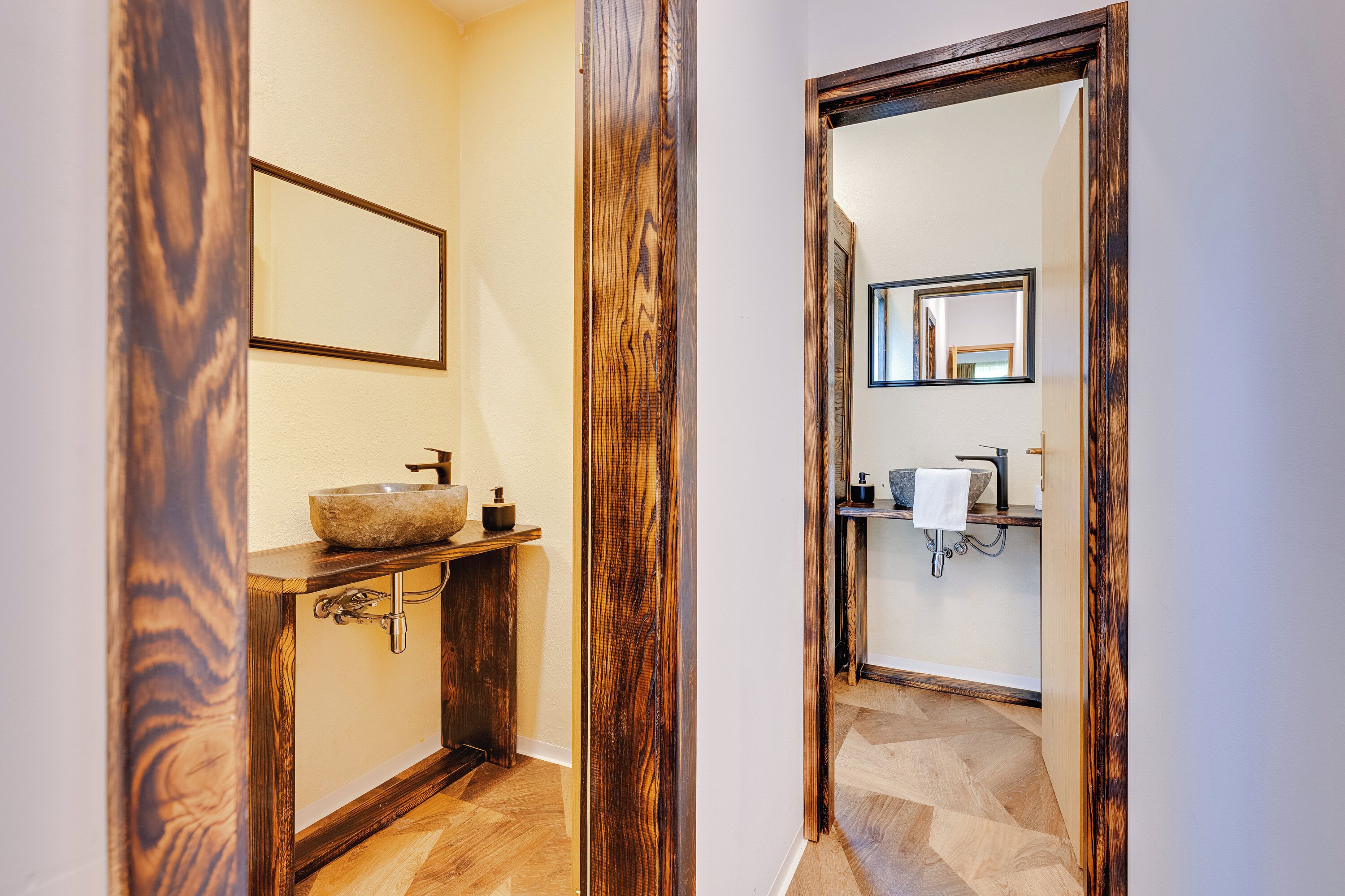 Un corridoio con pavimento in legno, un lavabo con bacino in pietra e uno specchio appeso al muro.