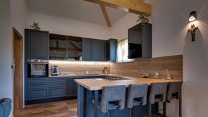 A modern kitchen with dark cabinets, a wooden countertop, and a bar area with stools. - Plitvice Nature Resort (Plitvička Jezera)