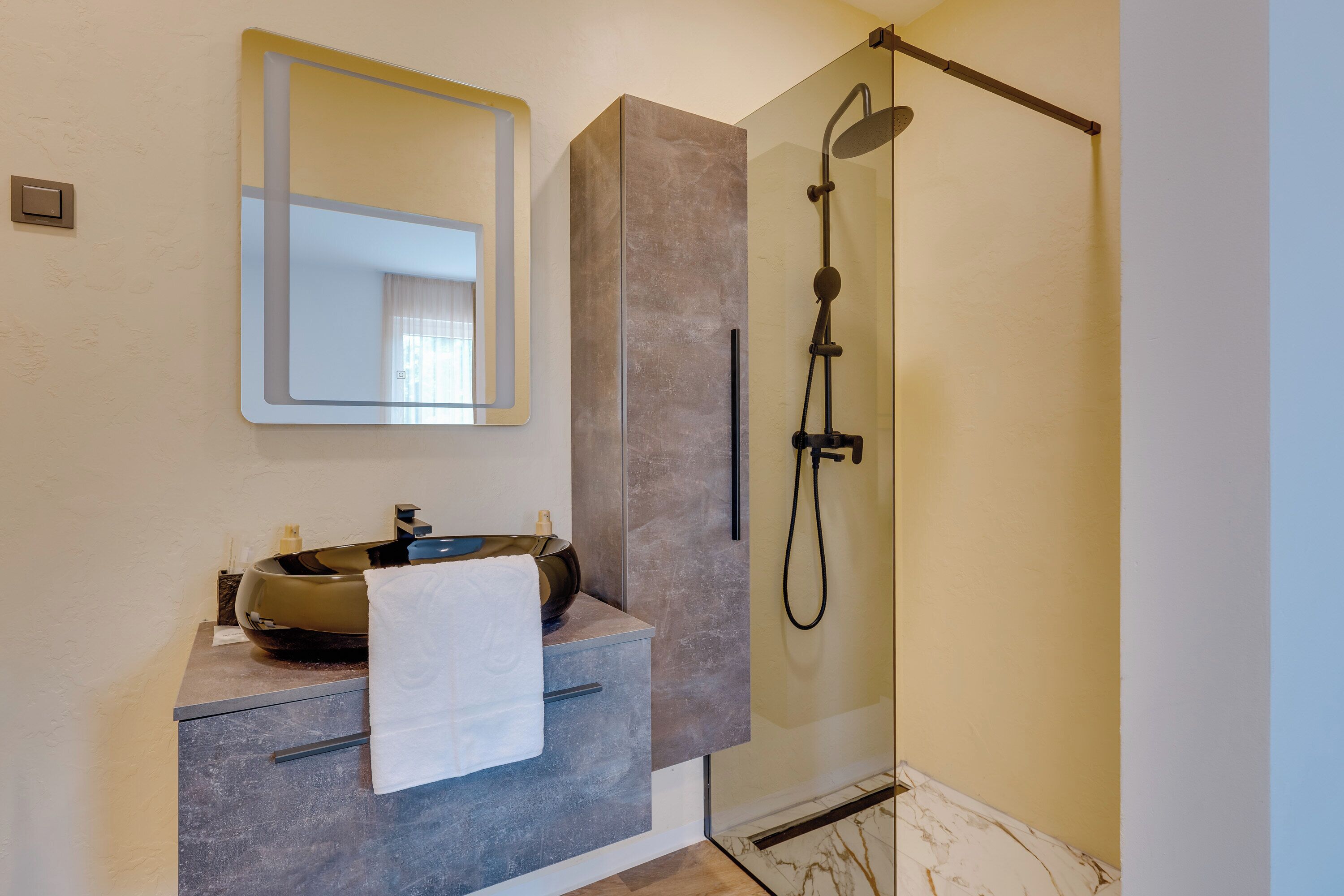Une salle de bain au design moderne, dotée d’un grand miroir, d’un lavabo rond et d’une douche à parois de verre.