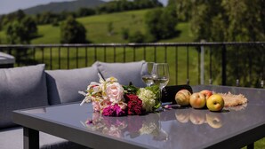 A table with a bouquet of flowers, two glasses of white wine, and several apples on a balcony overlooking a green landscape. - Plitvice Nature Resort (Plitvička Jezera)