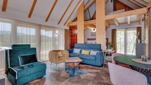 A spacious living area with a high ceiling, wooden beams, a blue sofa, a green armchair, and a dining table. - Plitvice Nature Resort (Plitvička Jezera)