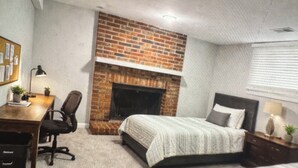 Une chambre avec une cheminée en briques, un lit, un bureau et une chaise.