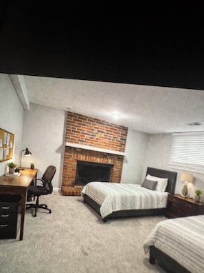 A bedroom with a brick fireplace, a bed, a desk, and a chair.
