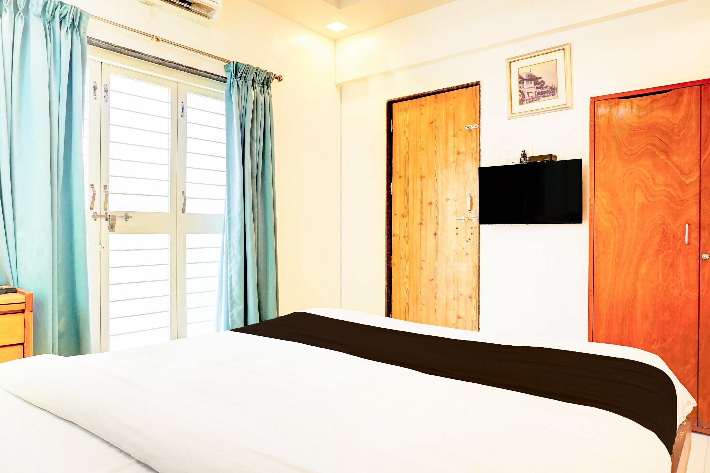 A bedroom with a bed, a wooden wardrobe, a door with a picture, and a flat-screen TV.