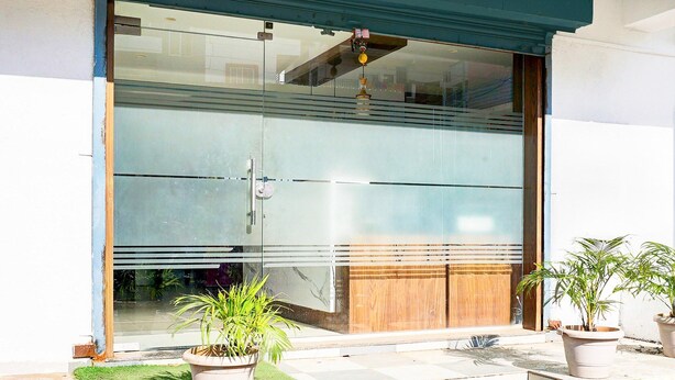 A modern building with a large sliding glass door, a wooden bench outside, and potted plants. - Classic With Balcony Ubale Nagar (Pune)