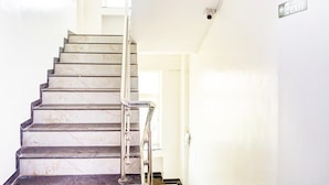 A marble staircase with a metal handrail leading to a door with an emergency exit sign. - Classic With Balcony Ubale Nagar (Pune)