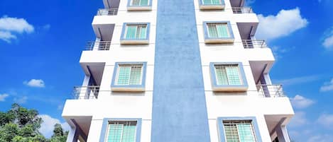 A multi-story building with a central vertical feature, balconies, and a sign indicating a company-serviced collection.