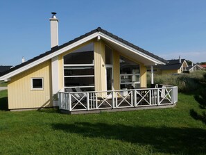 Ein eingeschossiges Gebäude mit Satteldach, einer überdachten Terrasse mit weißer Umlaufung und einem Schornstein.