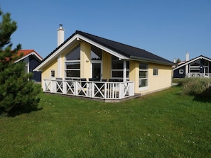 Eingeschossiges Haus mit Balkon, Schornstein und gepflegtem Rasen.