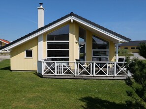 Ein gelbes Gebäude mit einem weißen Balkon, großen Fenstern und einem Schornstein.