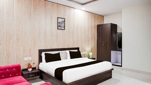 A modern bedroom with a large bed, a red chair, a wardrobe, and a small table with a vase. - Deluxe With Twin Bed Hotel Sky Inn (Lucknow)
