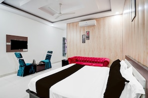 Quarto de hotel moderno com uma cama grande, um sofá vermelho, uma televisão de tela plana e um ventilador de teto.