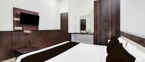 Quarto de hotel com uma cama, televisão presa na parede, espelho e guarda-roupa.