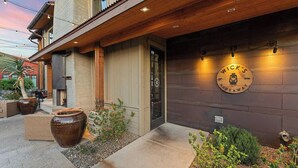 Un bâtiment à l’extérieur en bois, une grande enseigne circulaire portant le nom « WICK’S Hideaway », et des espaces de repos en plein air agrémentés de grands jardinières.
