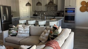 Un salon moderne avec un canapé beige, une cuisine avec des meubles blancs et un coin repas.
