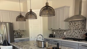 Une cuisine moderne dotée d’un îlot central, de tabourets de bar, de luminaires suspendus et d’un réfrigérateur en acier inoxydable.