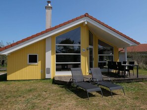 A yellow building with a red roof, large windows, and a covered outdoor seating area with chairs. - 4 Star Holiday Home in Grossenbrode (Grossenbrode)