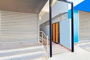 A modern building with a closed shutter door, a staircase with metal railings, and a blue wall. - Super Hotel O Yeshwanthpur (Bengaluru)