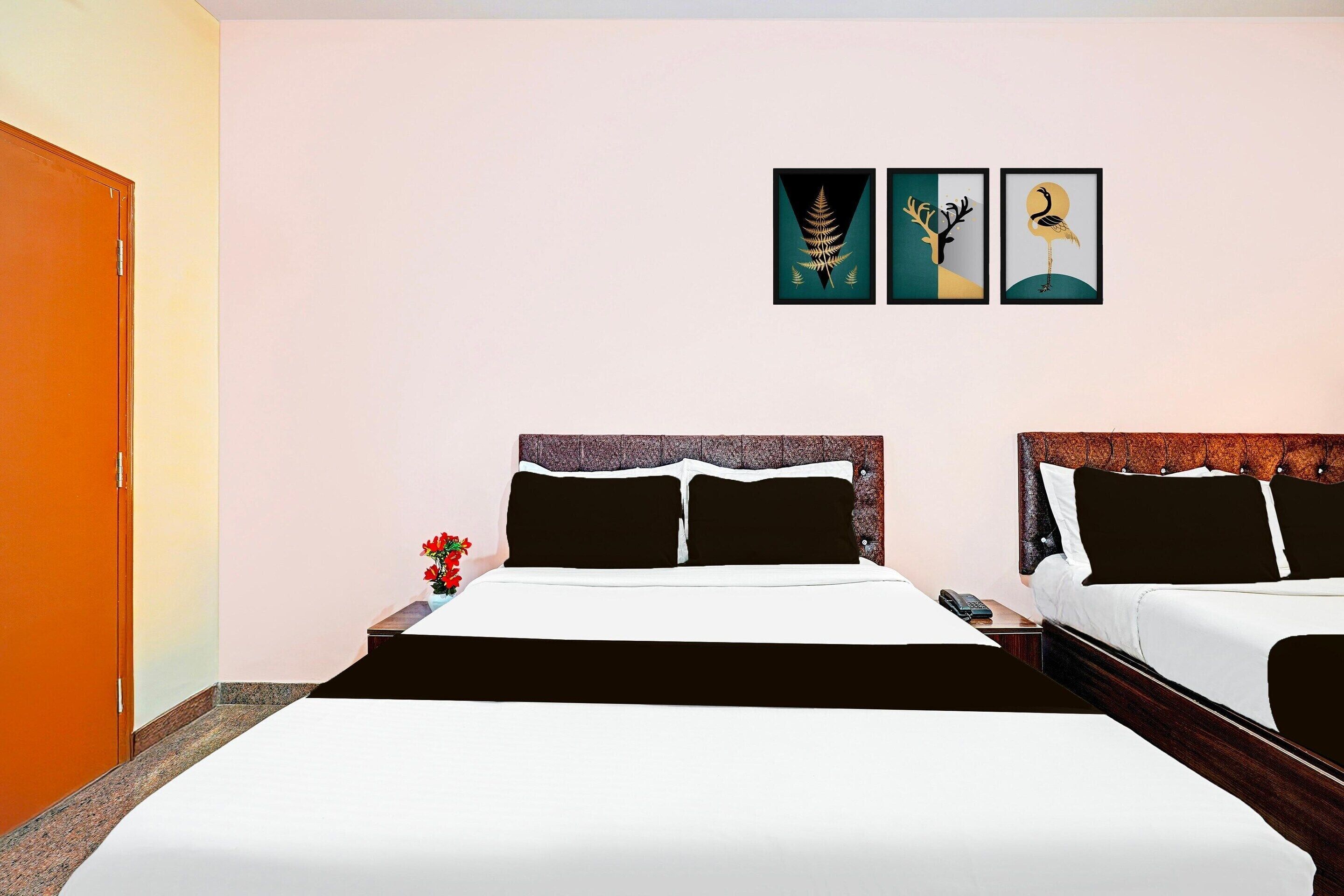 Ein Hotelzimmer mit zwei Betten, einem Nachttisch, einer Vase mit Blumen und drei gerahmten Kunstwerken an der Wand.