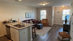 A modern kitchen with a central island, a dining area with a brown leather couch, and a living room with a television.
