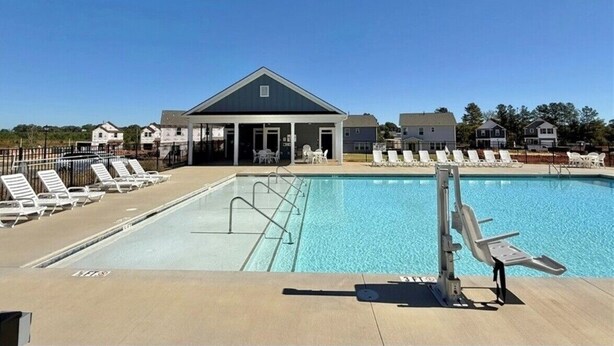 A swimming pool with lounge chairs, a covered seating area, and a building with a gabled roof.
