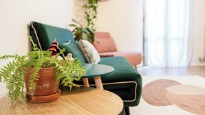 En stue med en grøn sofa, et rundt træbord og en potteplante.