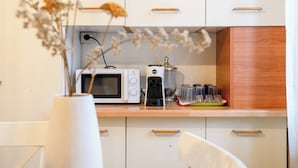Et køkken med hvide skabe, en mikrobølgeovn, en kaffemaskine og en vase med visne blomster.