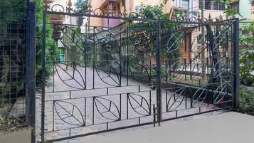 Une entrée fermée par un portail en métal décoratif, un chemin pavé et des immeubles résidentiels en arrière-plan.