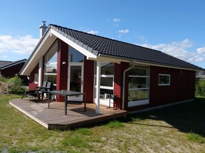 A red building with a sloped roof, large windows, and a wooden deck with outdoor furniture. - 4 Star Holiday Home in Grossenbrode (Grossenbrode)