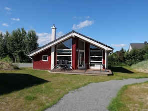Ein rotes Haus mit einem großen Glasbalkon, einem Schornstein und einer Terrasse mit Gartenmöbeln.