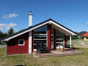 Ein rotes Gebäude mit einer großen Glasdoor, einem Schornstein und einer kleinen Terrasse mit Gartenmöbeln.