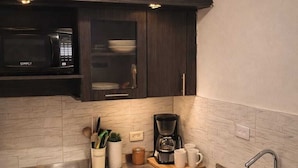 Cocina compacta con armarios oscuros, estufa de acero inoxidable, microondas, cafetera y pileta.